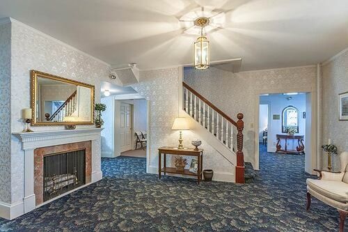 Funeral home interior with fireplace, staircase, blue patterned carpet, and chandelier.