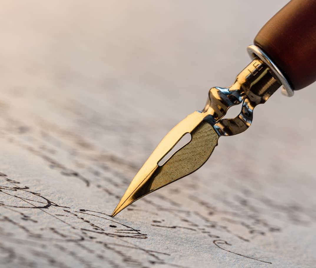 Close-up of a gold nib pen writing on aged paper with black ink.