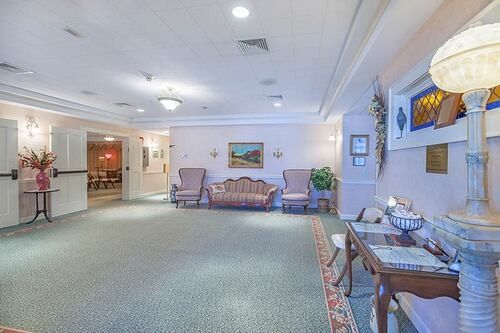 Lobby with light pink walls, green carpet, antique furniture, and a large decorative lamp.