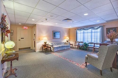 Waiting area with sofa, chairs, and window with curtains; neutral colors and soft lighting.