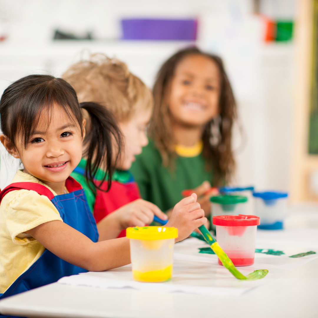 A group of children are sitting at a table playing with paint