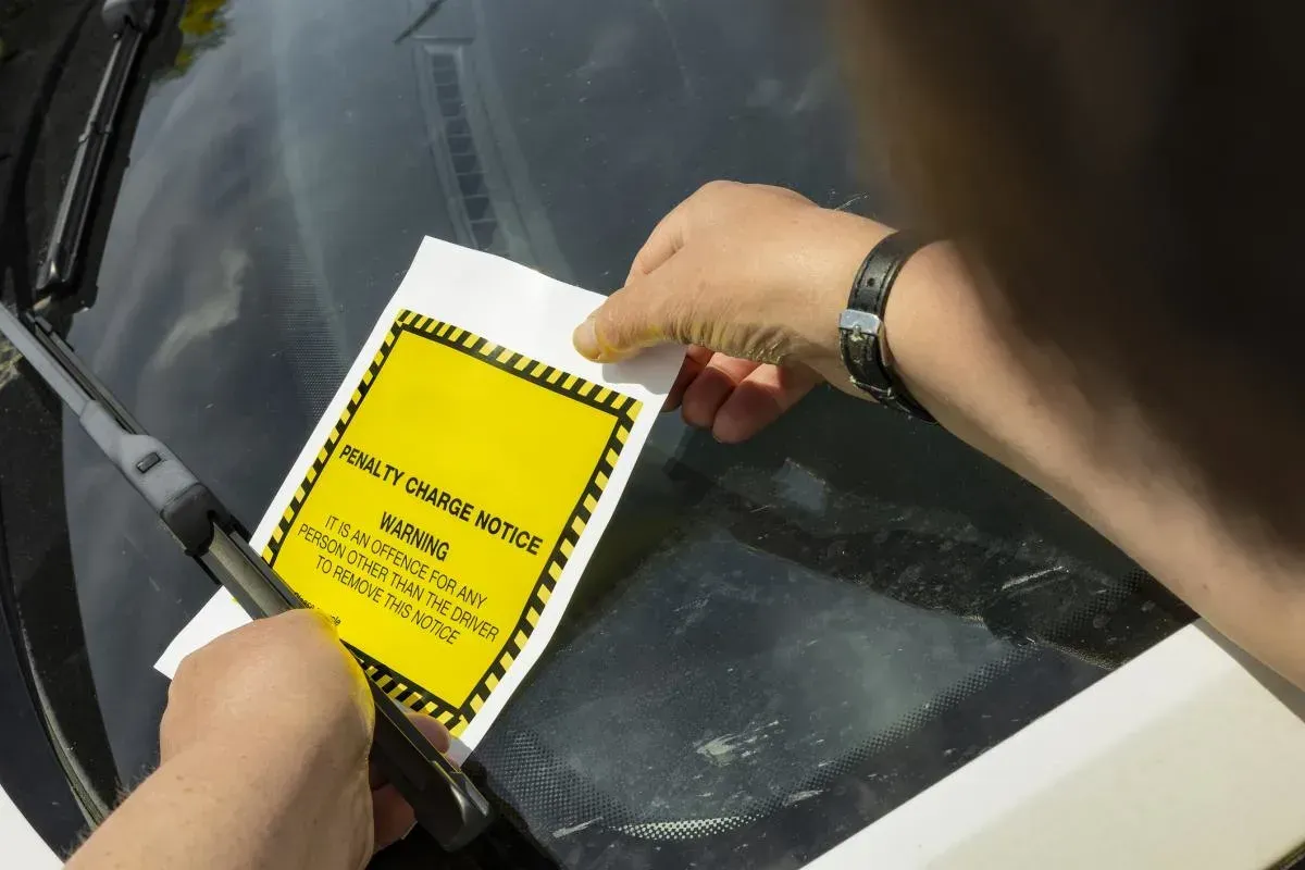 Person placing a yellow parking violation sticker on a car windshield.
