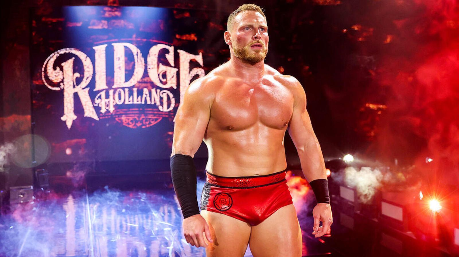 Ridge Holland in wrestling gear, red trunks, standing in a spotlighted wrestling ring entrance, a WWE stage background.
