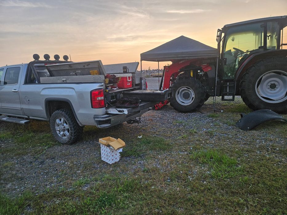 Silver truck towing a tractor at dusk, with a work setup.