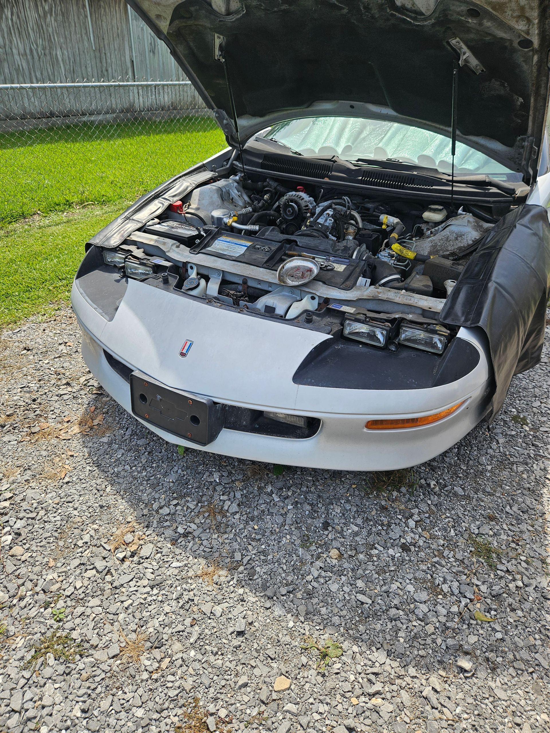 White car with hood open, parked on gravel, engine visible.