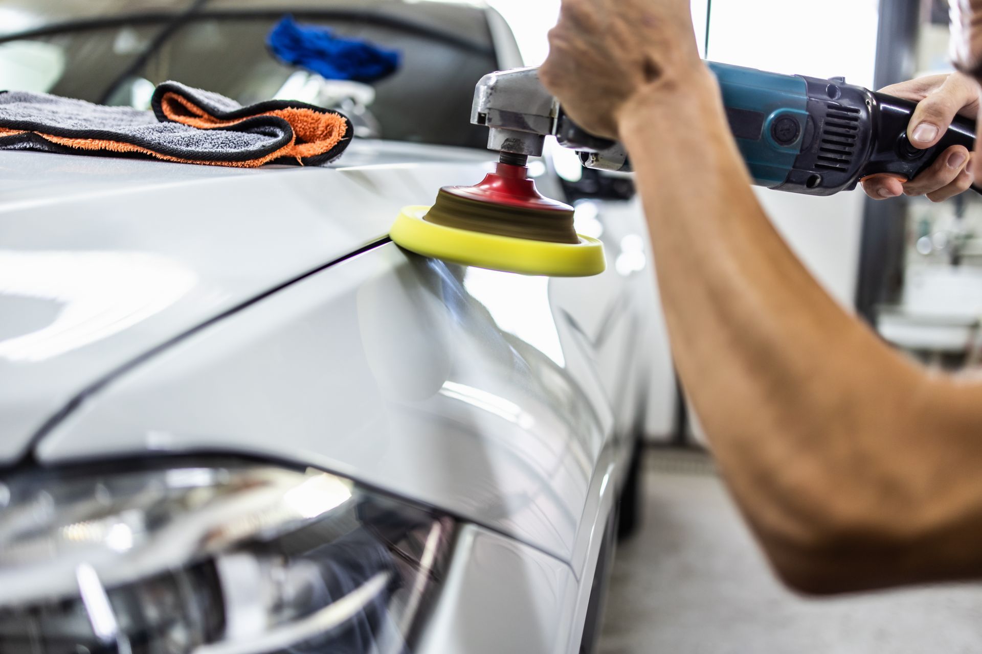Person polishing a white car with a power buffer.