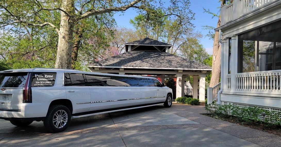 A long white limousine parked next to a gazebo and a house with a porch. The scene is outdoors in daylight.