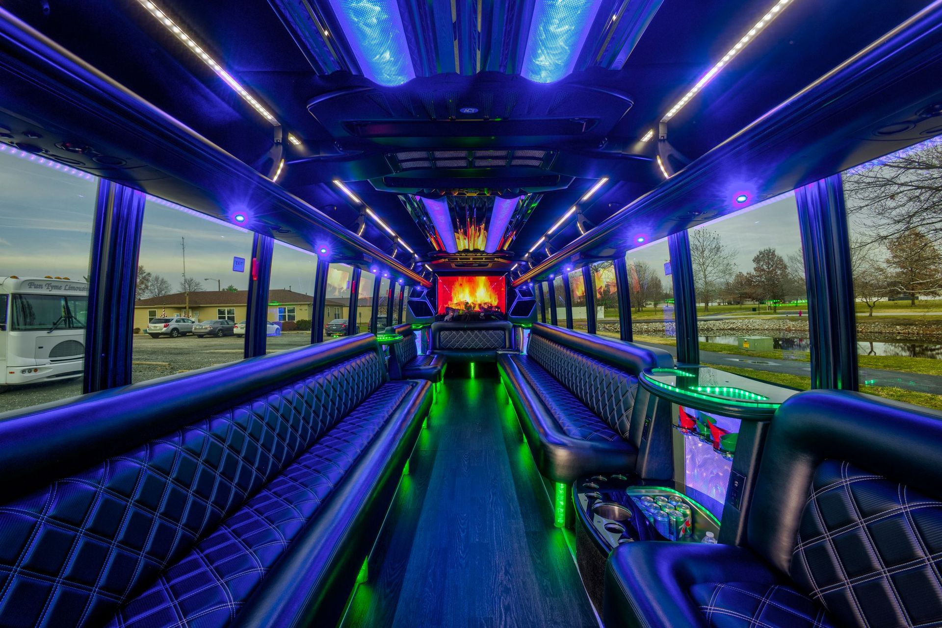 Inside of a party bus, showcasing long seating with vibrant blue and green LED lights.