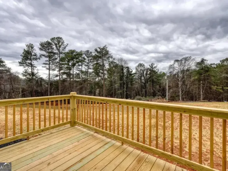 A view from a wooden deck looking out over a grassy field toward a line of pine trees under a cloudy sky.