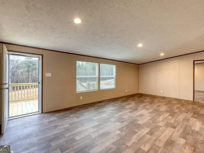 An empty room with tan walls, recessed lighting, wood-look flooring, and a glass door leading to a wooden deck.
