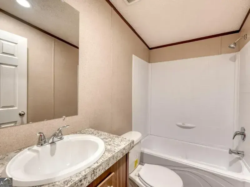 A beige bathroom featuring a white vanity with a sink and mirror next to a white tub and shower combo.