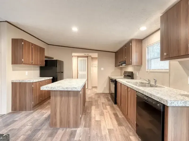 A modern kitchen with brown wood cabinets, granite-patterned countertops, a central island, and black appliances.