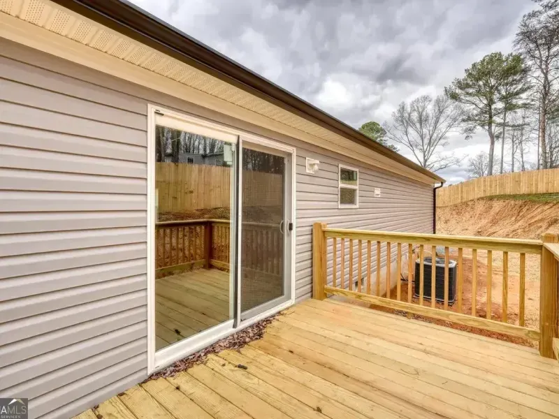 A light-colored vinyl house exterior with a sliding glass door and a wooden deck featuring a railing and an HVAC unit.