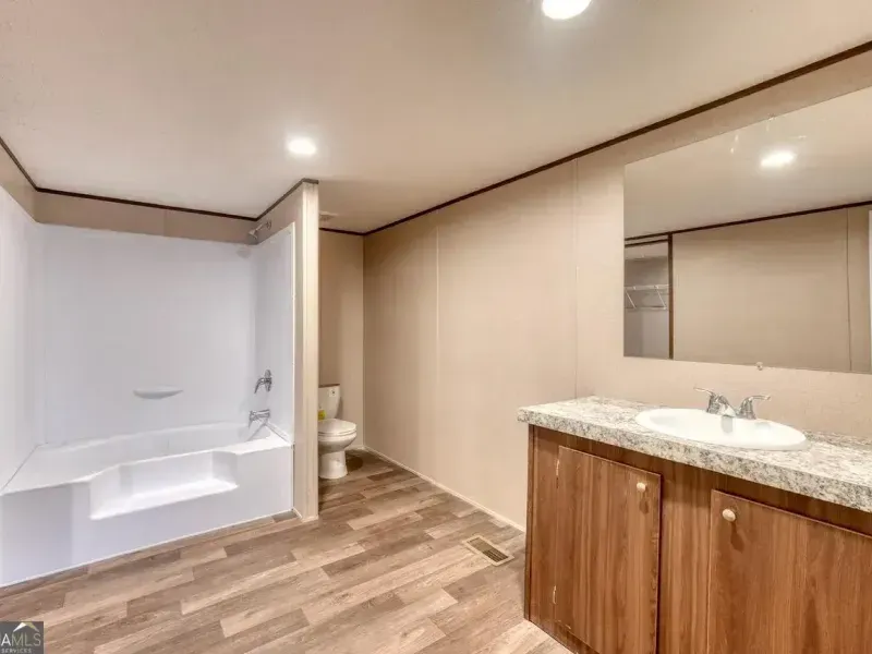 A modern bathroom featuring a white soaking tub, a toilet tucked in a corner, and a wood vanity with a white sink.