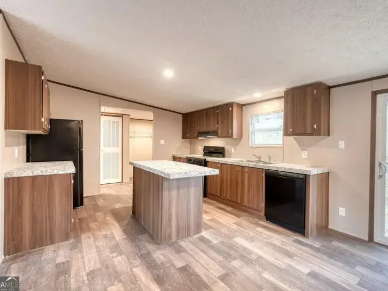 A modern kitchen with brown wood cabinets, granite-look countertops, an island, and black appliances.