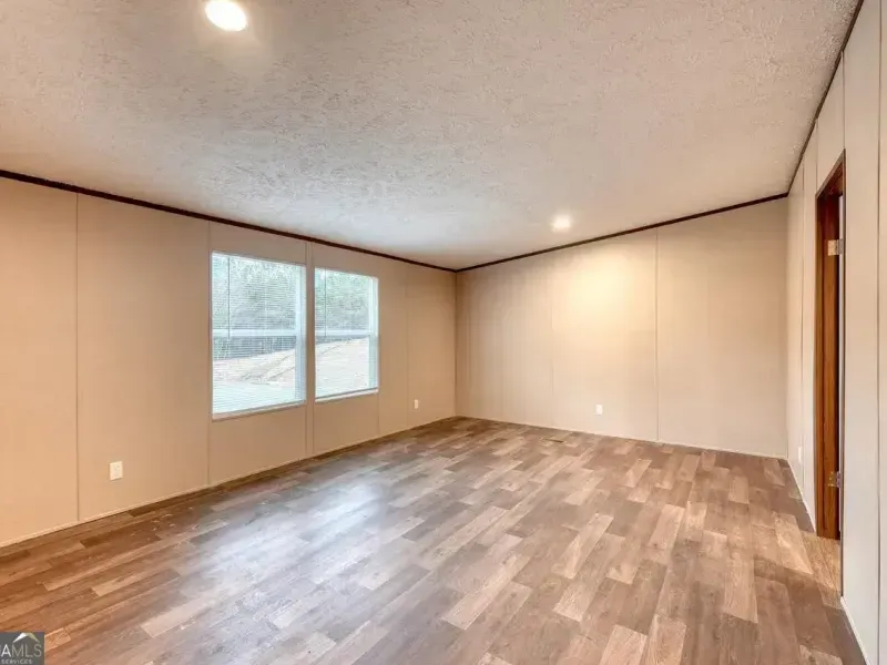 An empty room with light tan walls, wood-look flooring, two windows on the left, and a doorway on the right.