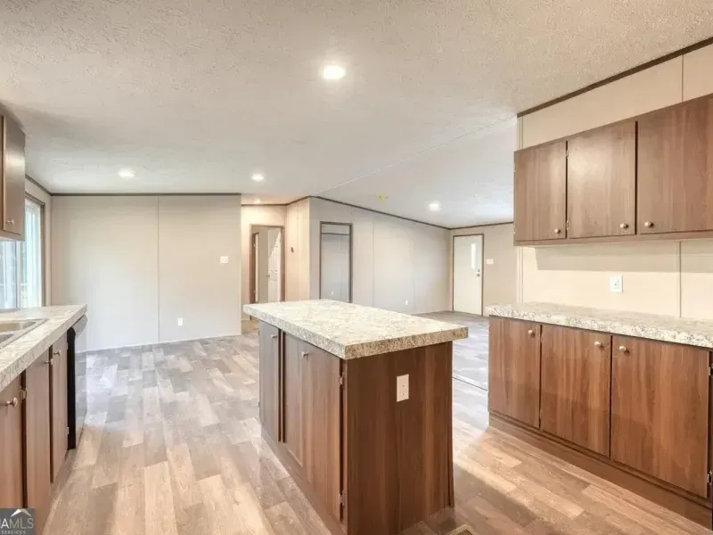 A kitchen with brown wooden cabinets, light granite countertops, a center island, and wood-patterned flooring.