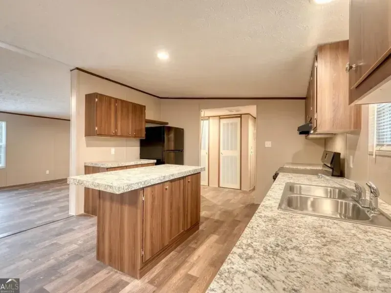A modern kitchen with brown cabinets, a granite-topped island, and light wood flooring in an open-concept layout.