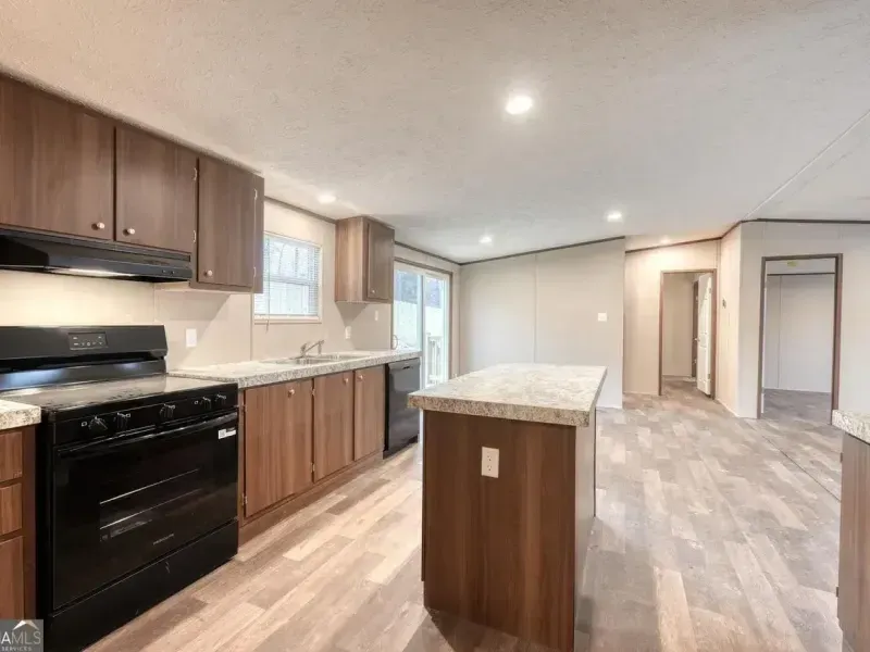 A modern kitchen with brown cabinets, a black stove, a kitchen island with a stone countertop, and wood-look flooring.