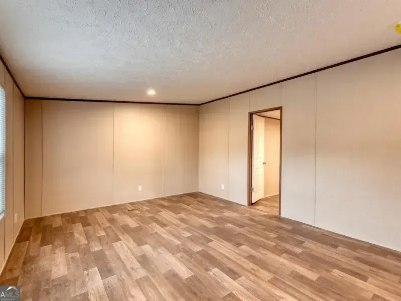 A spacious, empty room featuring light-colored walls, a textured ceiling, and wood-patterned flooring with a doorway.