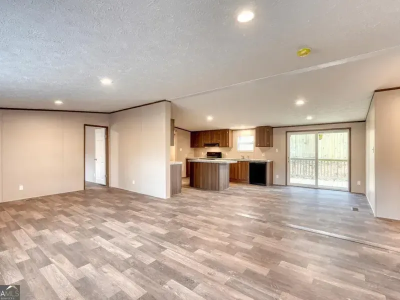 Open-concept living room with light wood-look vinyl flooring, beige walls, a central kitchen island, and a sliding door.