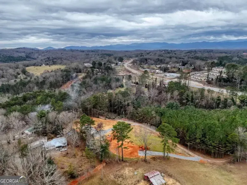 Aerial view of a clearing with red dirt, surrounding forest, and distant mountains under a cloudy sky.