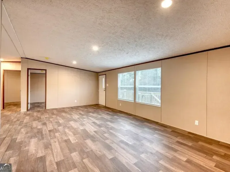 Empty room with wood-look laminate flooring, beige walls, a window, and two doorways.