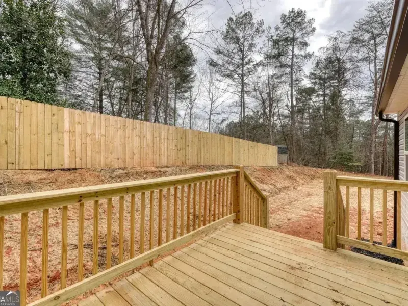 A wooden deck overlooks a sloped, bare dirt yard enclosed by a tall, new wooden privacy fence backed by pine trees.