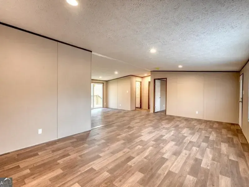 An open-concept living area with light-toned walls, wood-look flooring, recessed ceiling lights, and two doorways.