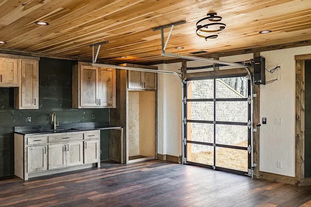 A kitchen area with wooden cabinets, dark countertops, and a wood-plank ceiling, adjacent to a glass garage door.