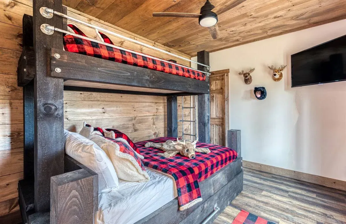 A rustic bedroom features a dark wood bunk bed with red plaid bedding, matching ceiling, and animal decor on white walls.