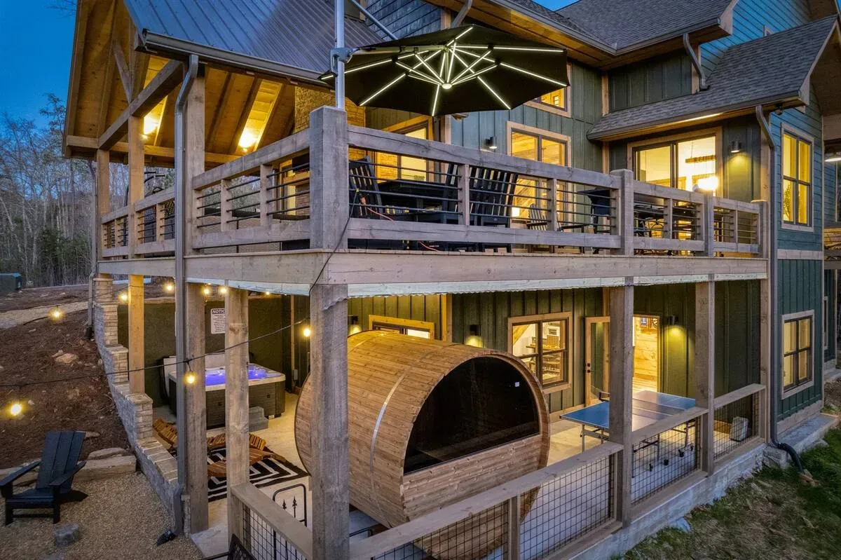 Two-story house with a balcony featuring patio furniture, a hot tub, a barrel sauna, and a ping-pong table on the patio.