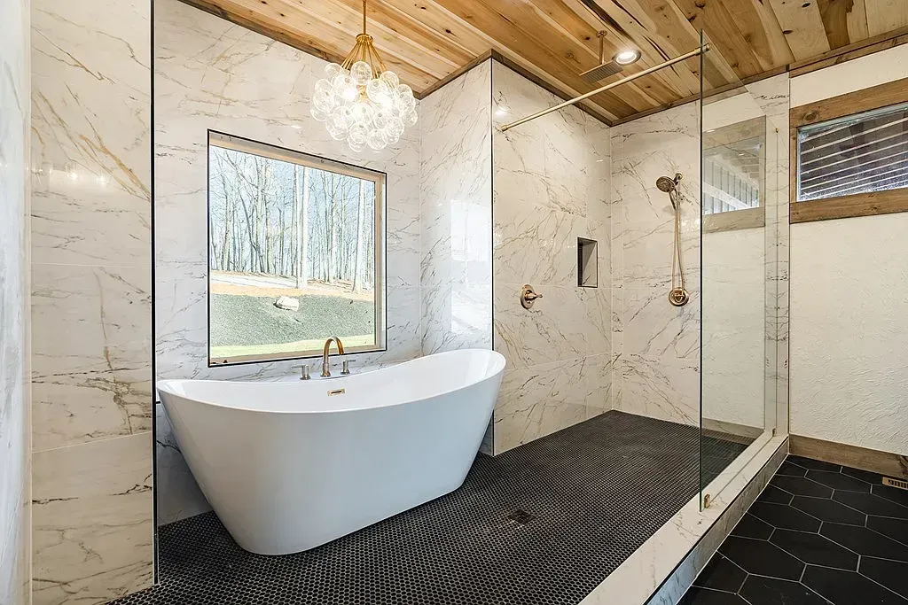 Modern bathroom featuring a white soaking tub, walk-in glass shower, marble walls, and a wood-paneled ceiling.