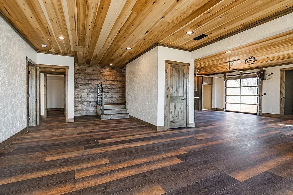 A rustic interior featuring wooden ceilings, textured white walls, a stone accent wall, and a garage-style glass door.