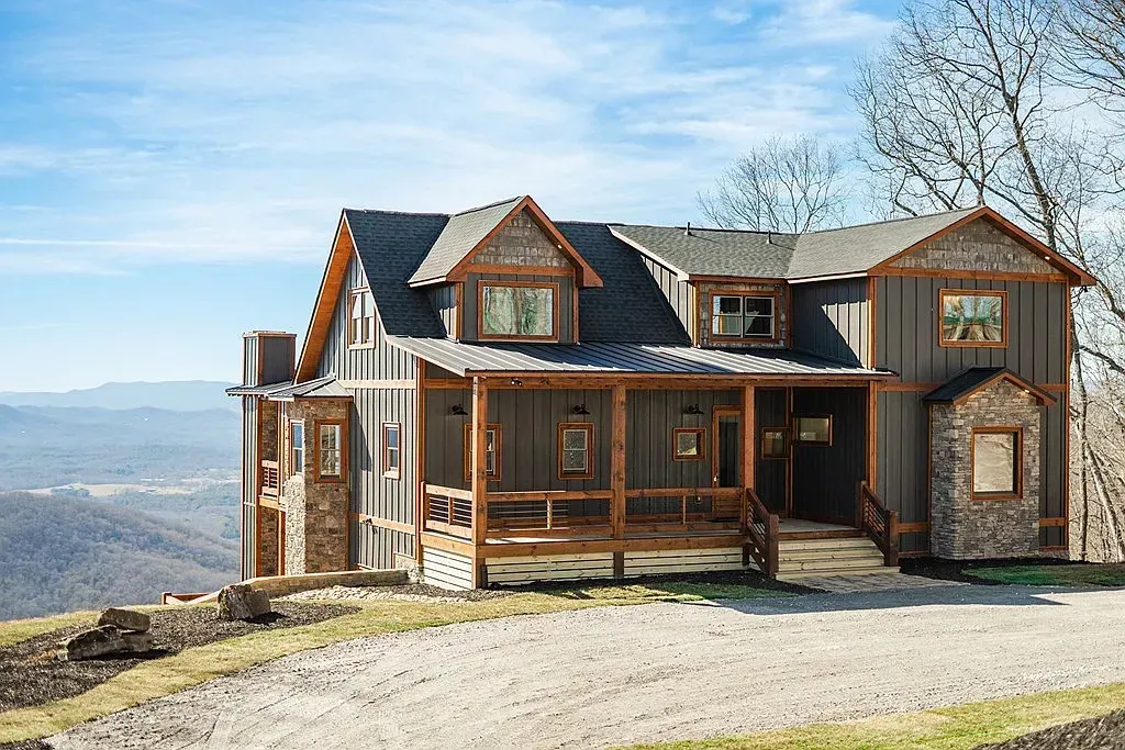 A two-story mountain home with dark board-and-batten siding, stone accents, and a front porch overlooking a valley.