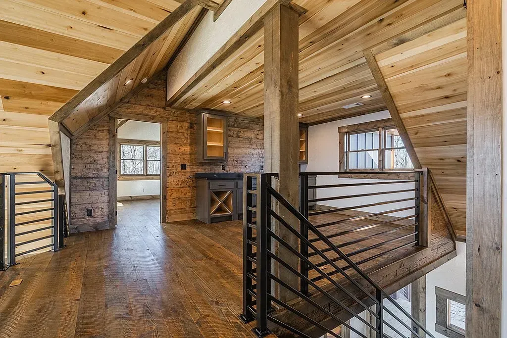 A rustic loft landing with wood paneled walls, ceiling, and floors, featuring a dark metal railing overlooking the stairs.