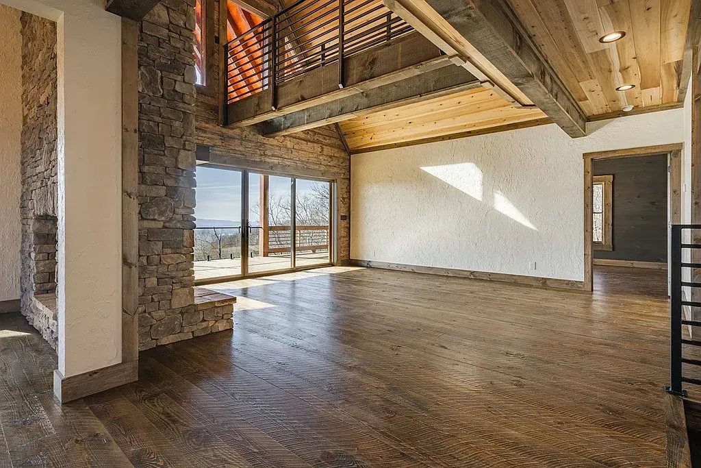 Spacious rustic room featuring stone walls, polished floors, wood ceilings, and large windows with a view.