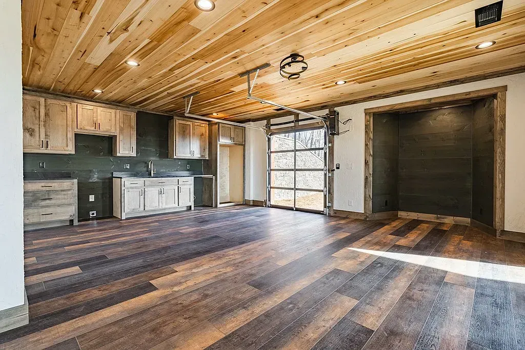 A rustic-style room featuring wood-paneled ceilings, dark flooring, wooden cabinets, and a glass-paneled garage door.