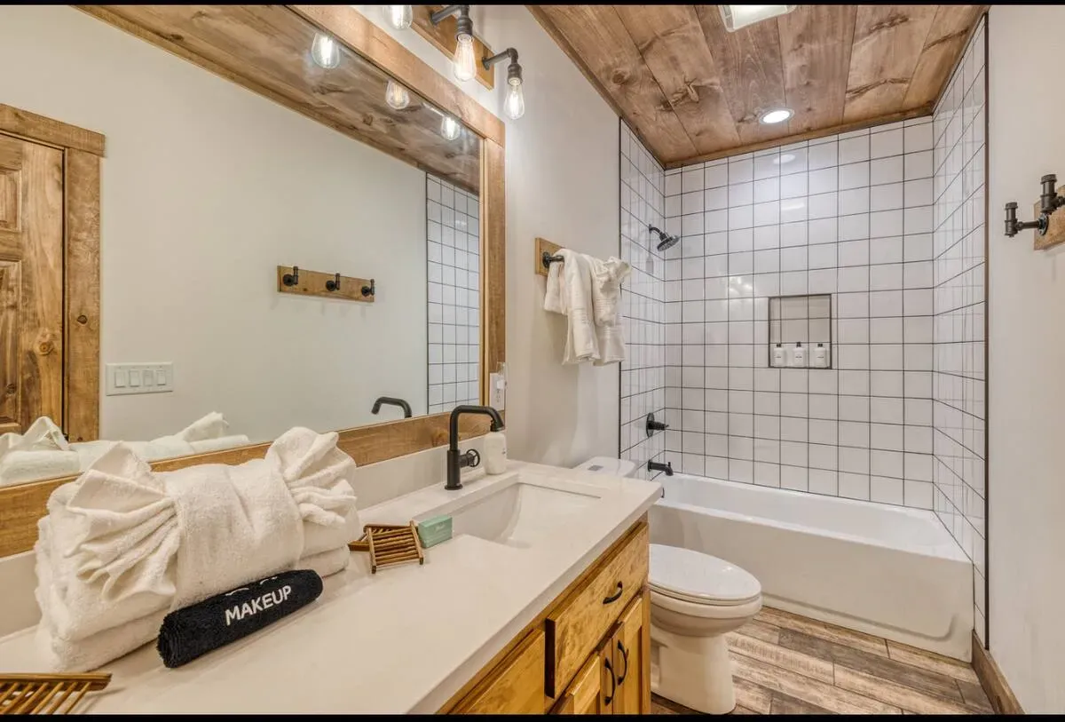 A rustic-style bathroom features wood-trimmed mirrors, a white subway-tile tub shower, and a wooden vanity cabinet.