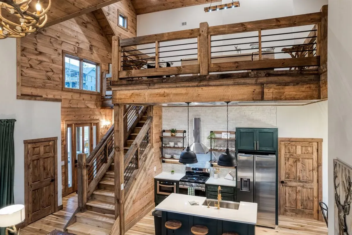 A rustic interior featuring a two-story open-concept kitchen with wooden walls, stairs, and an upstairs loft balcony.