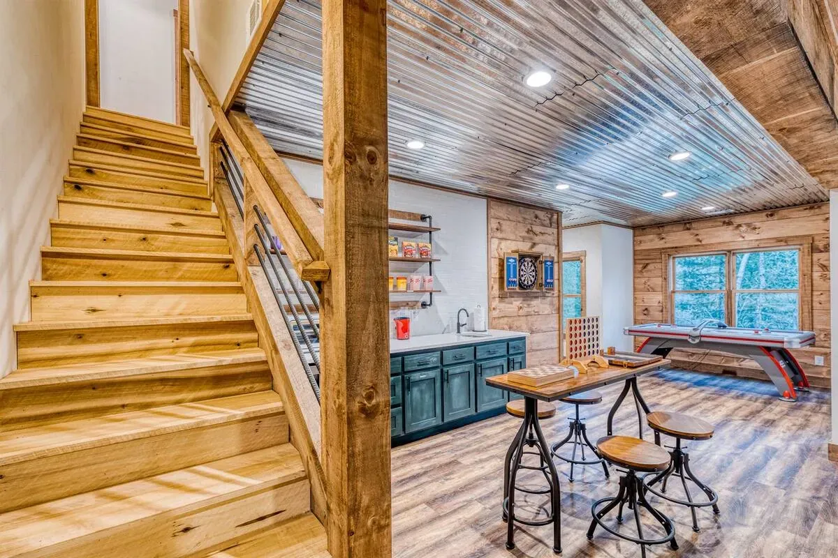 A rustic basement room features wooden stairs, a corrugated metal ceiling, a blue kitchen counter, and a dining table.