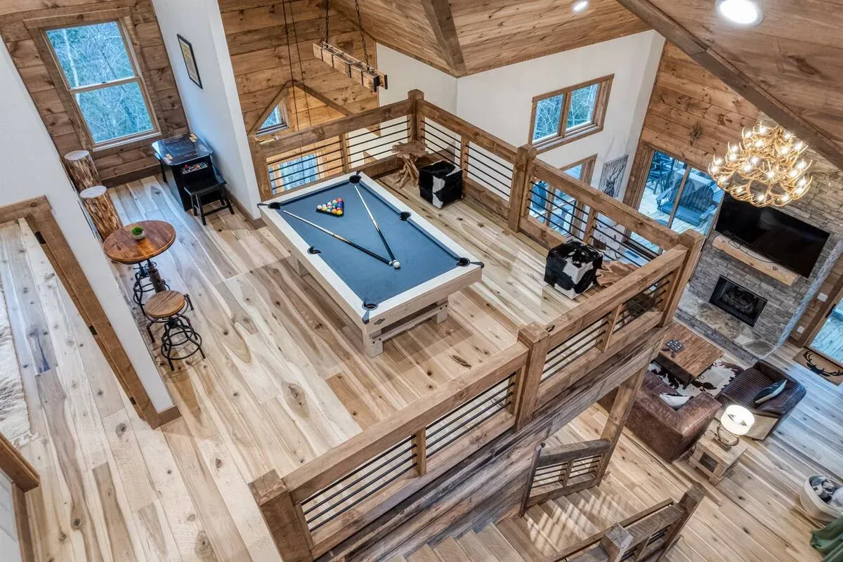 A high-angle view of a rustic wooden loft featuring a billiards table, overlooking a lower living area with a fireplace.