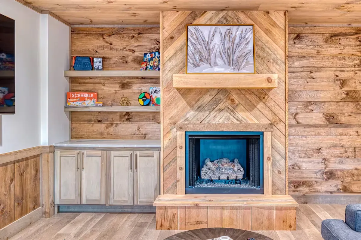 A fireplace with a chevron-patterned wood surround, stone hearth, and light wood built-in cabinets with shelving.
