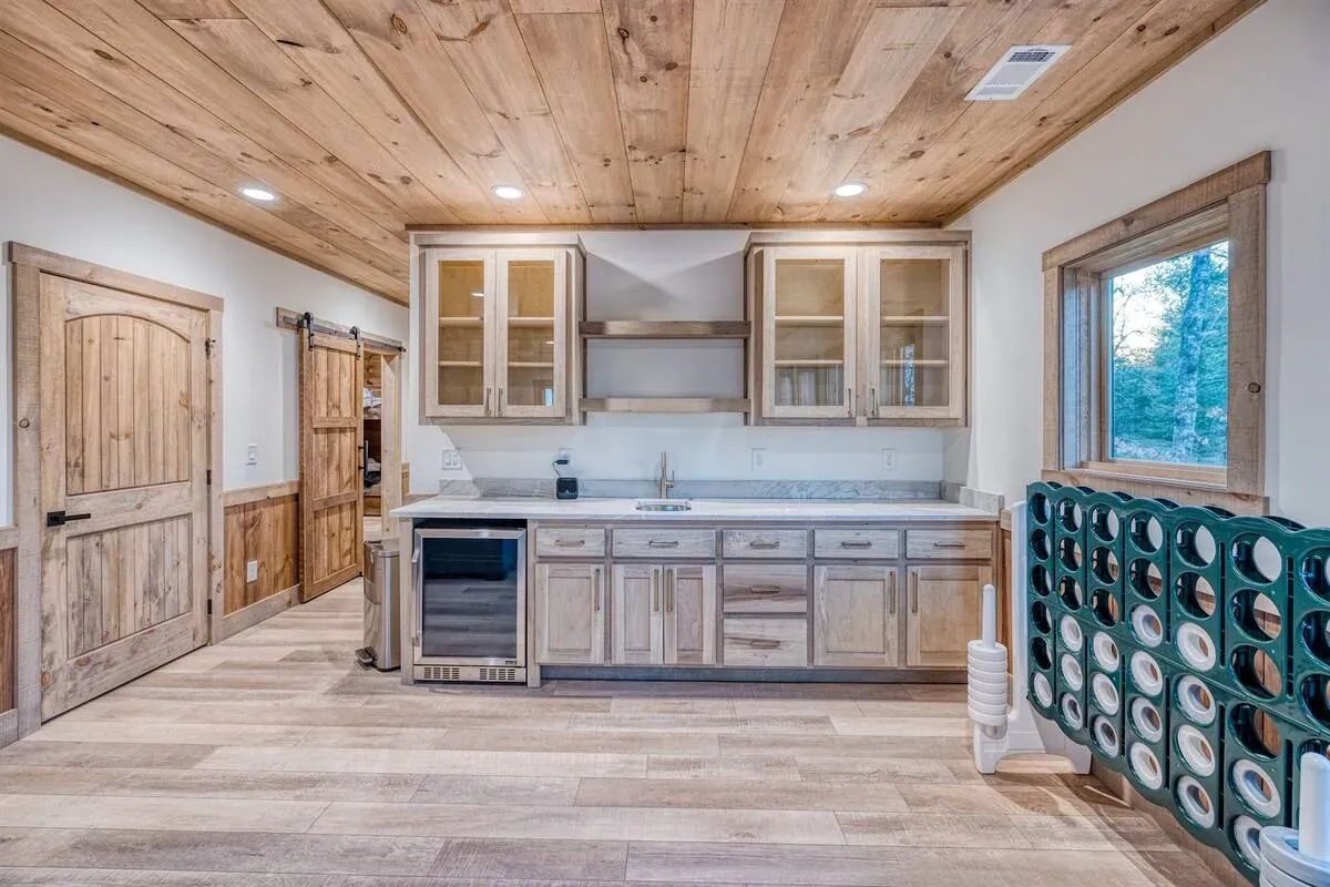 Rustic kitchenette with light wood cabinets, wood-paneled ceiling, sliding barn doors, and a green Connect Four game.