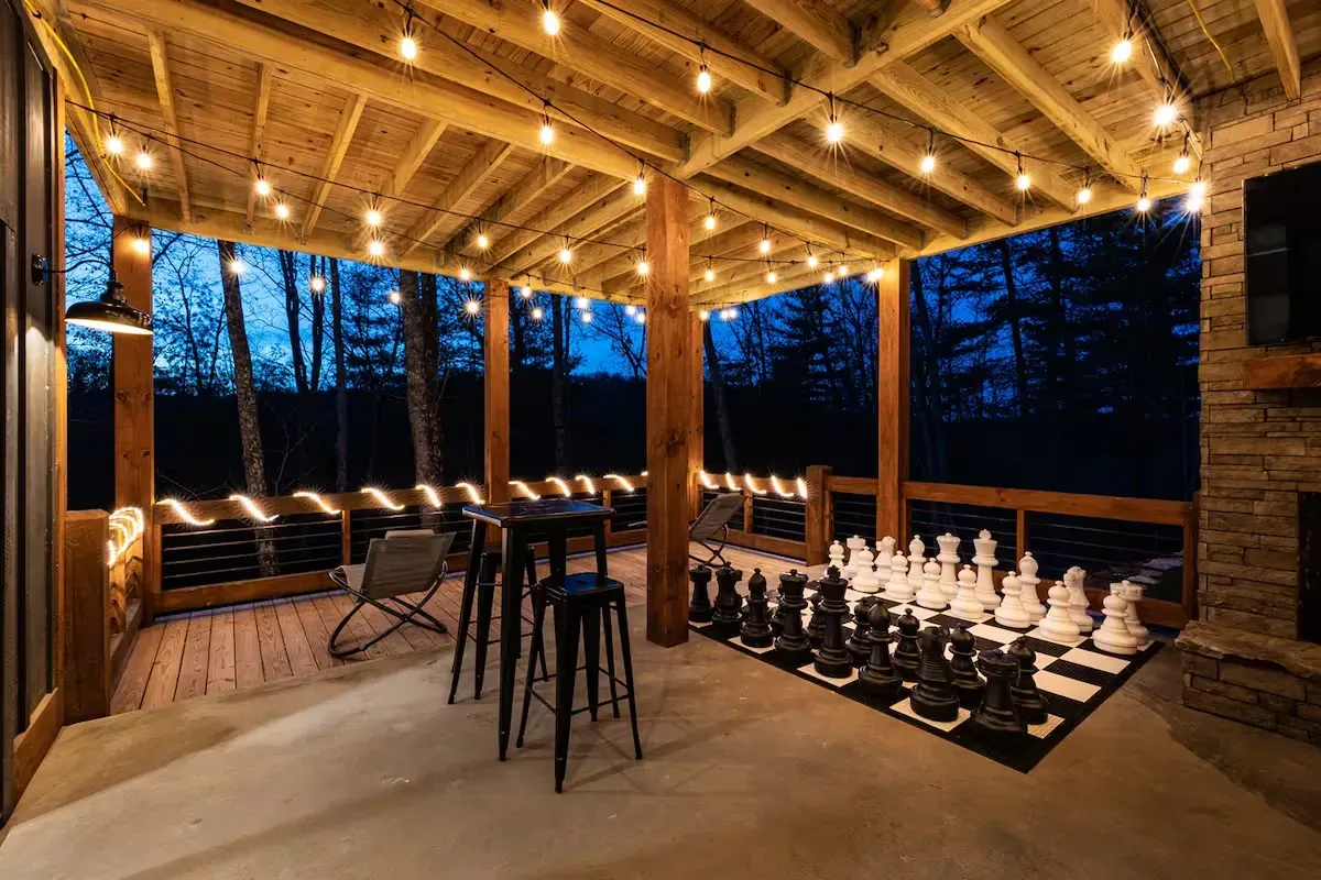 Outdoor covered patio at twilight with a giant chess set, high-top bistro table, and string lights overhead.