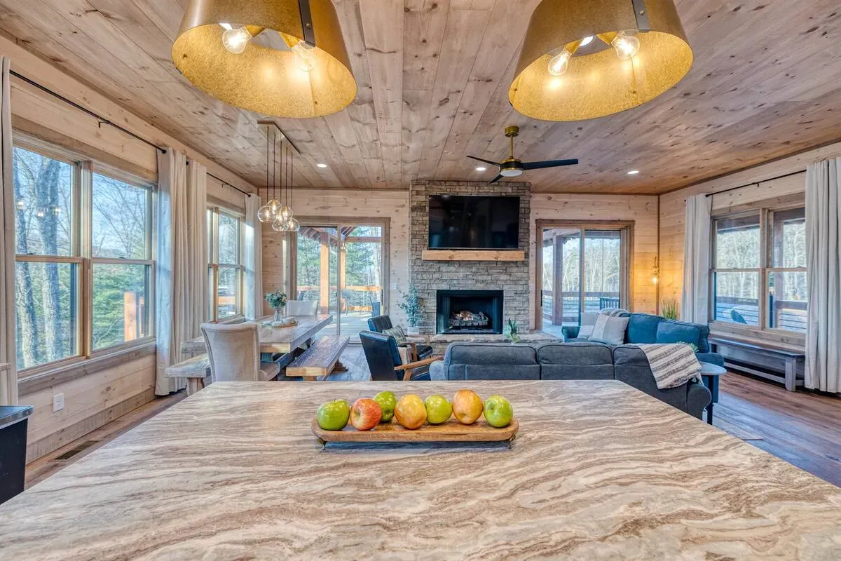 A view from a kitchen island featuring a bowl of fruit, overlooking an open-plan living room with wood ceilings and decor.