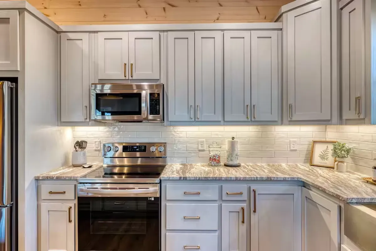 A kitchen with light gray cabinets, stainless steel appliances, a tile backsplash, and stone countertops.