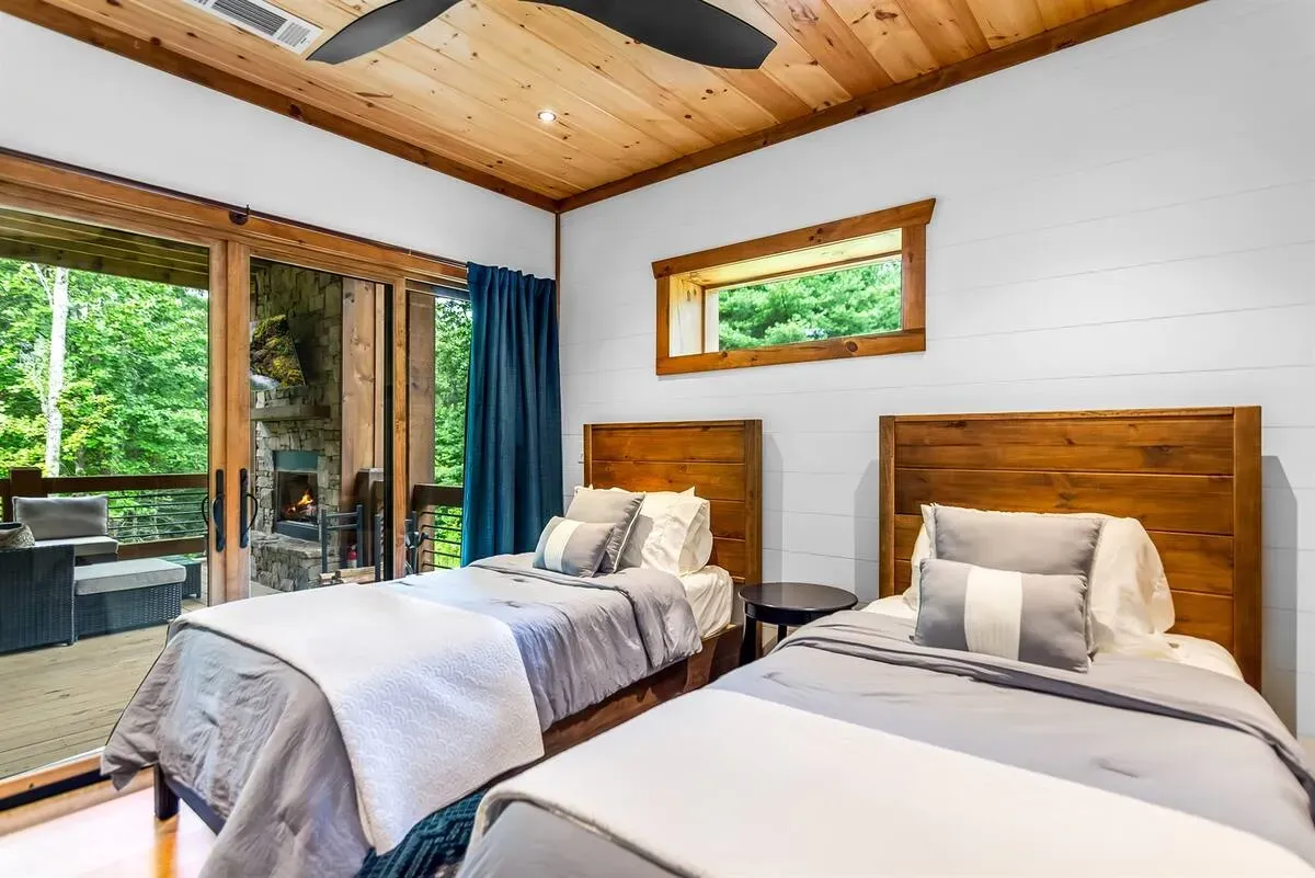 A bedroom with two twin beds featuring wood headboards, white bedding, gray accents, and sliding doors opening to a deck.
