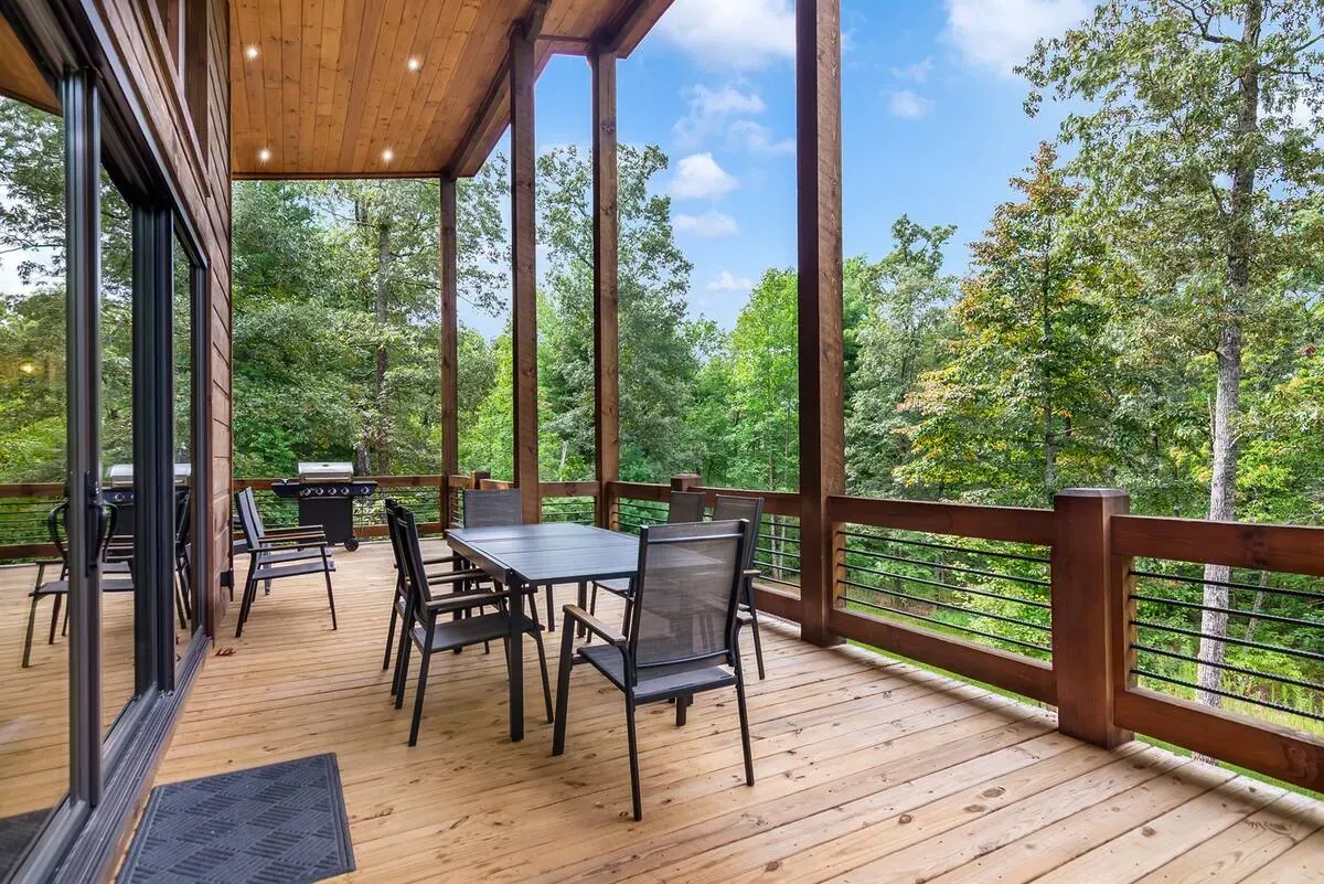 A wooden deck with patio furniture and a grill overlooking a lush green forest under a blue sky.