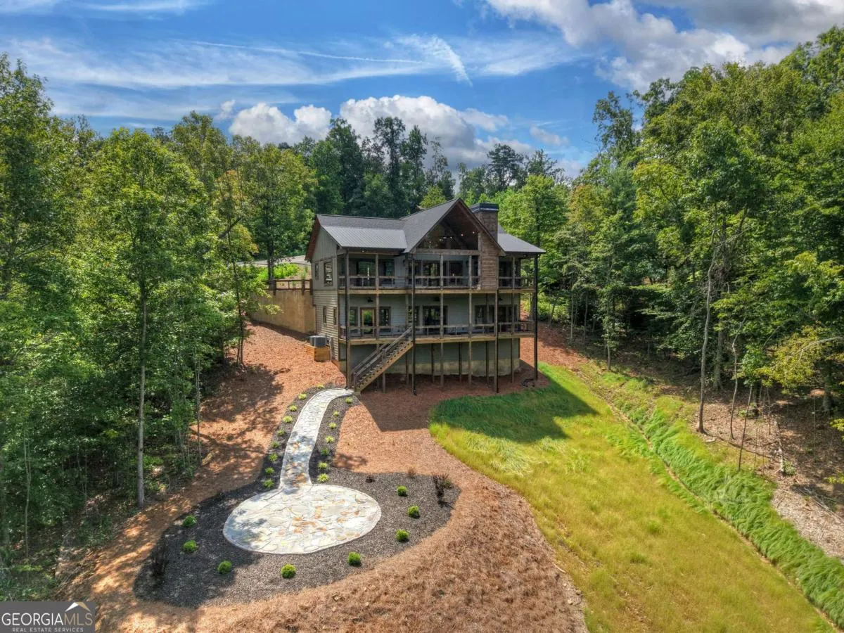 A multi-story wooden cabin nestled in a lush, green forest with a stone walkway leading to a circular patio.